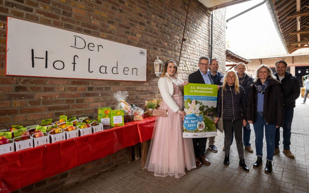 Gruppe vor dem Schild „Der Hofladen“ bei der Vorstellung des Meckenheimer Blütenfestes, mit der Blütenkönigin und Vertretern der Stadt