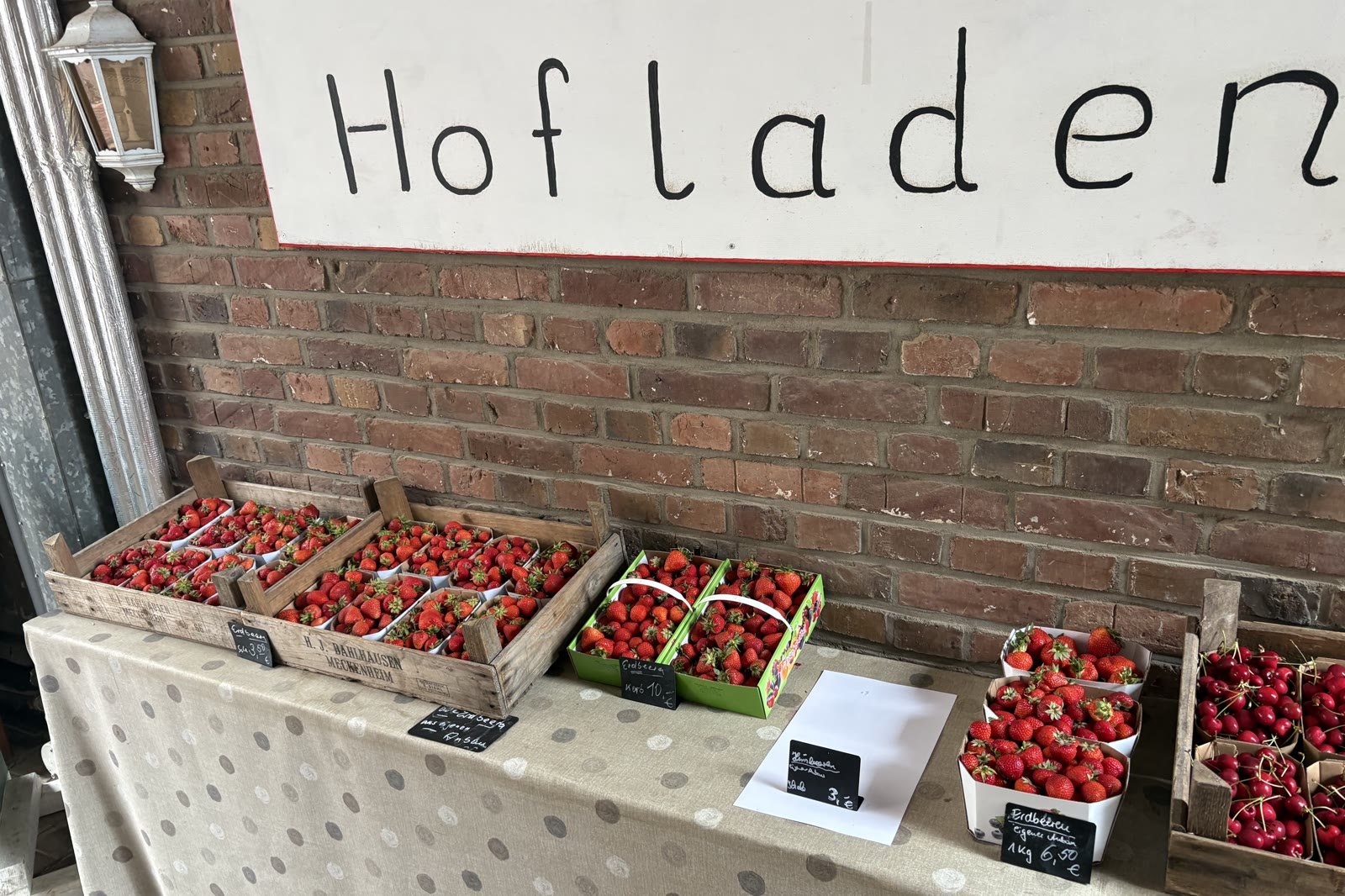 Holzkisten voller Erdbeeren und Kirschen auf der Theke unter dem handgeschriebenen Schild „Hofladen“
