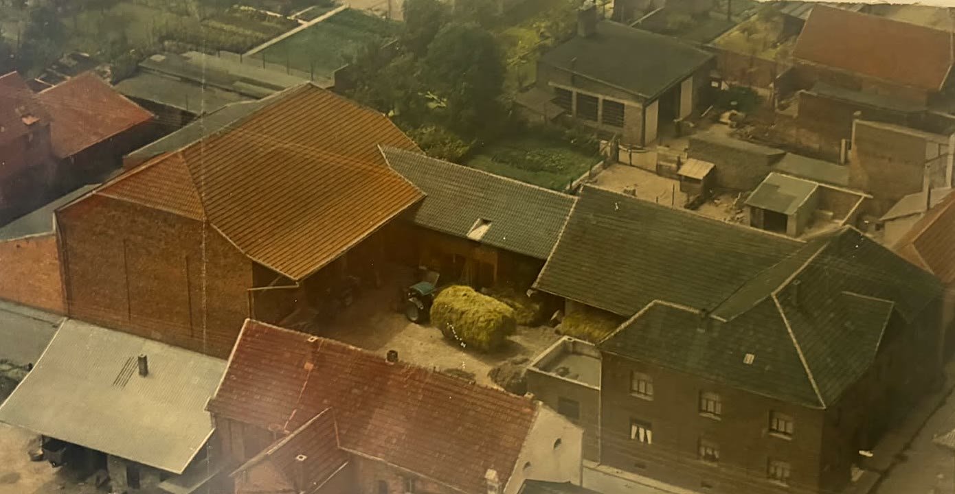 Altes Luftbild des Hofes: die Hofeinfahrt zwischen Scheune und Wohnhaus, im Innenhof ein Traktor und ein Wagen mit Heu