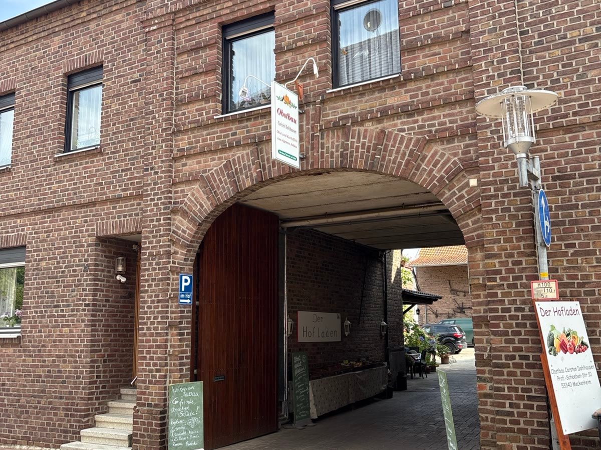 Der erste Hofladen in der Professor-Scheeben-Straße 10: die Toreinfahrt des Backsteinhofes mit dem Aufsteller „Der Hofladen“