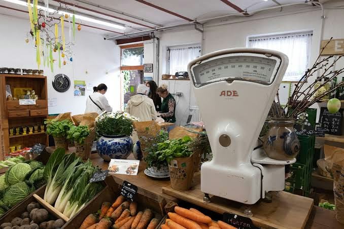 Alte Tafelwaage im Hofladen, davor Kisten mit Möhren, Salat und Kräutern